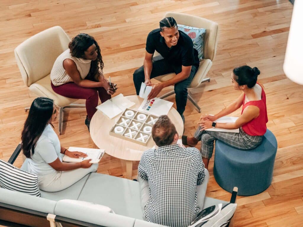 a group of colleagues sit on arm chairs and a sofa around a table, with notepads, in conversation