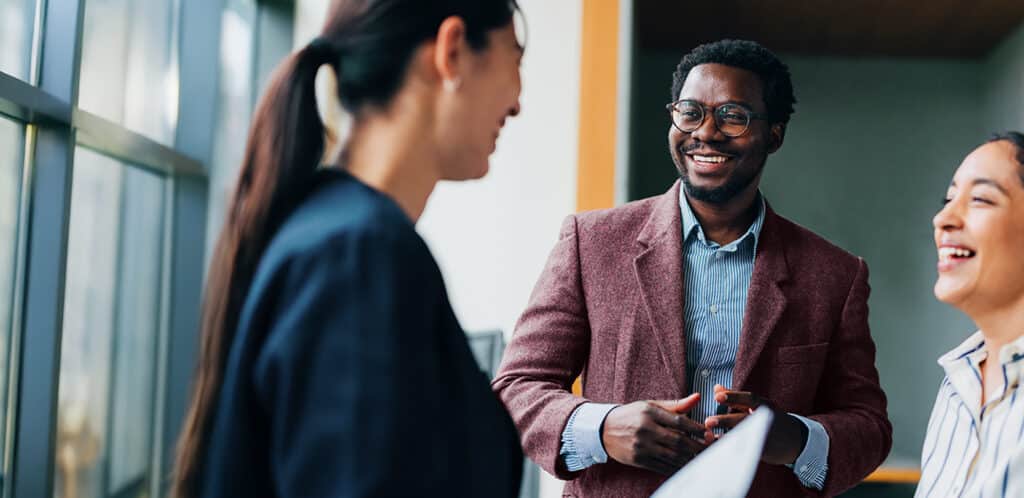 Three professionals share a light-hearted moment during a collaborative meeting, showcasing teamwork and a positive workplace atmosphere in a modern office environment.